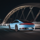 A blue 2023 Porsche 911 Carrera T drives on LA's new 6th Street Bridge at night.